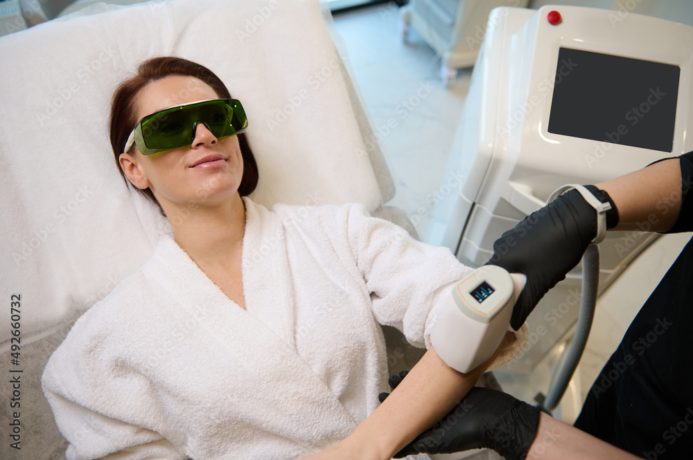 Fototapeta premium Middle aged beautiful Caucasian woman undergoing epilation procedure on hands in beauty salon. Body Care. Laser Hair Removal. Epilation Treatment. Smooth Skin.