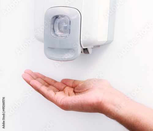 HANDS UNDER A AUTOMATIC WALL MOUNTED SANITISER DISPENSER.