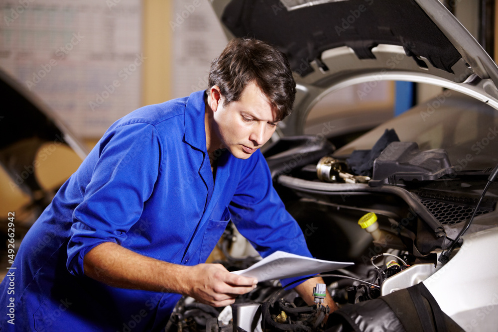 Id better check the wiring. A male mechanic reading some papers while working on the motor of a car. Id better check the wiring. A male mechanic reading some papers while working on the motor of a car.