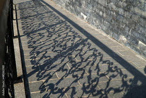 Shadows of a forged rustic iron fence on a stone-ground at outside