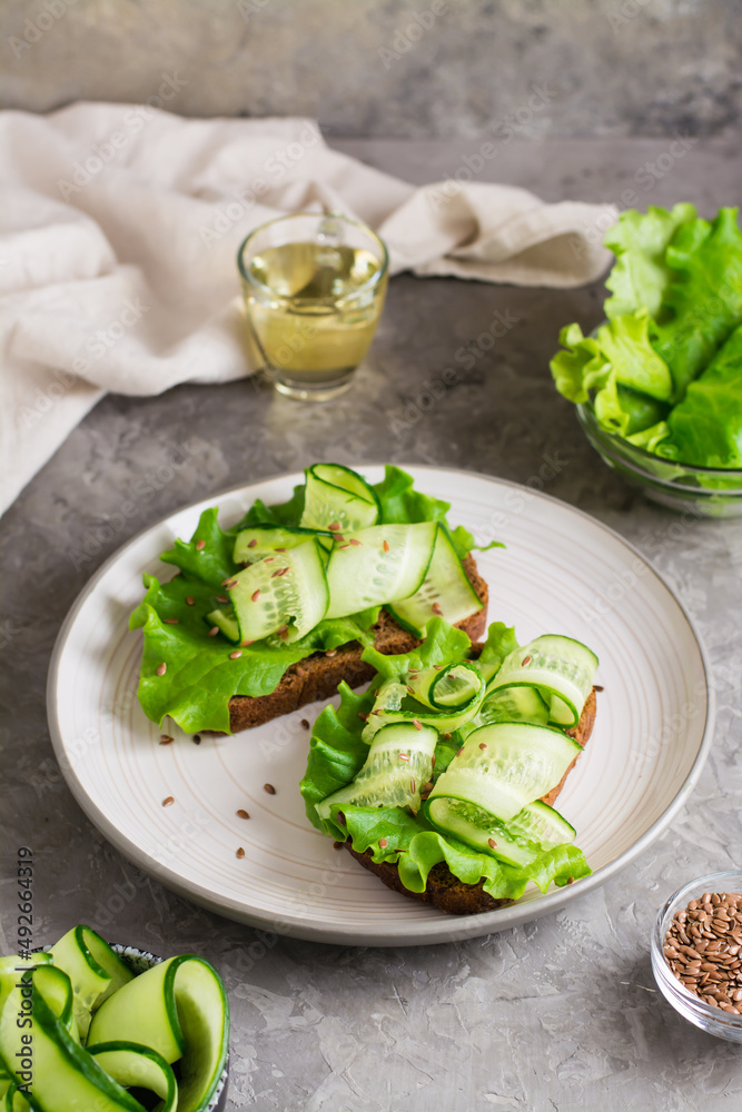 Ready-to-eat sandwiches with lettuce, cucumber and flax seeds on rye bread on a plate on the table. Healthy diet food. Vertical view