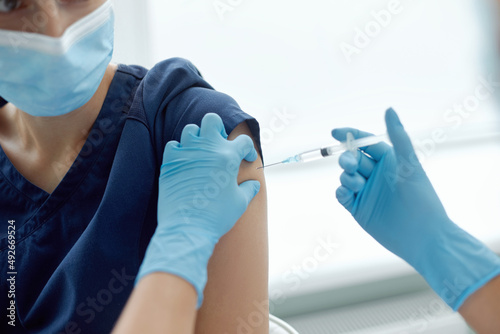 Woman in medical face mask getting injection at hospital. Doctor or nurse preparing syringe to give shot to female patient  concept of inoculation