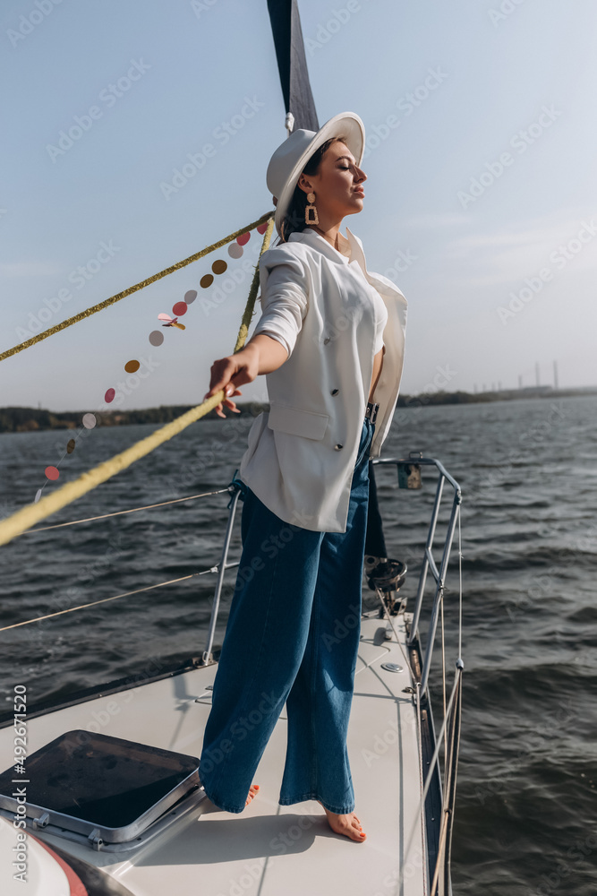 beautiful young woman in a hat stands on a yacht