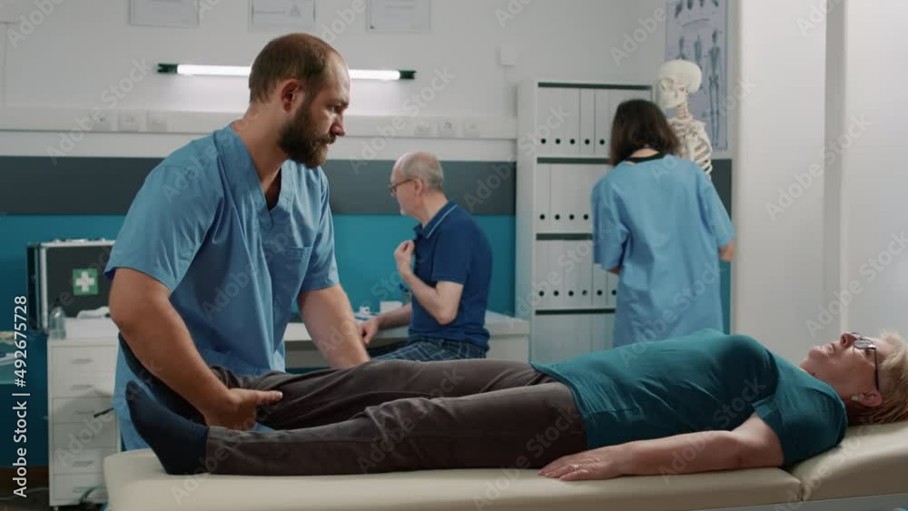 Physician doing legs raise exercise to stretch legs for old patient with mechanical disorders in rehabilitation cabinet. Osteopathy specialist doing physical therapy procedure to cure woman.