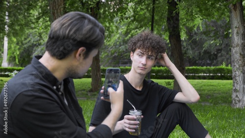 A guy takes pictures on the phone of another guy in nature in the summer. LGBT