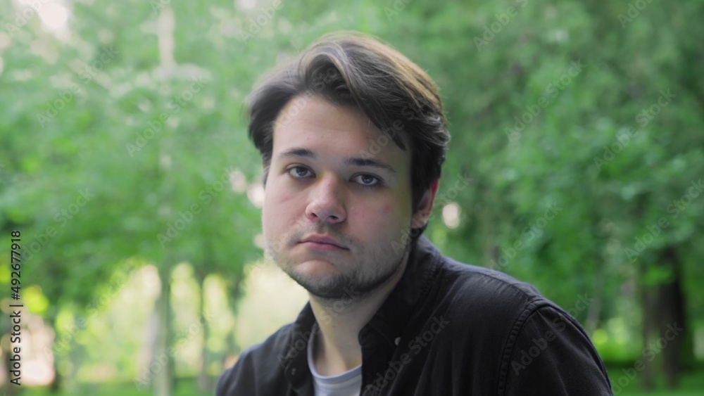 A young handsome guy looks sadly at the camera in nature in the summer A young handsome guy looks sadly at the camera in nature in the summer