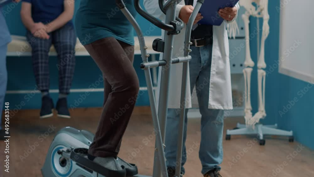 Old patient using stationary bicycle at physical therapy with physician