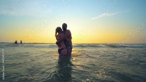 Happy cheerful young couple having fun in the sea at sunset, silhouette of couple enjoying together on a tropical beach on romantic vacation, honeymoon photo