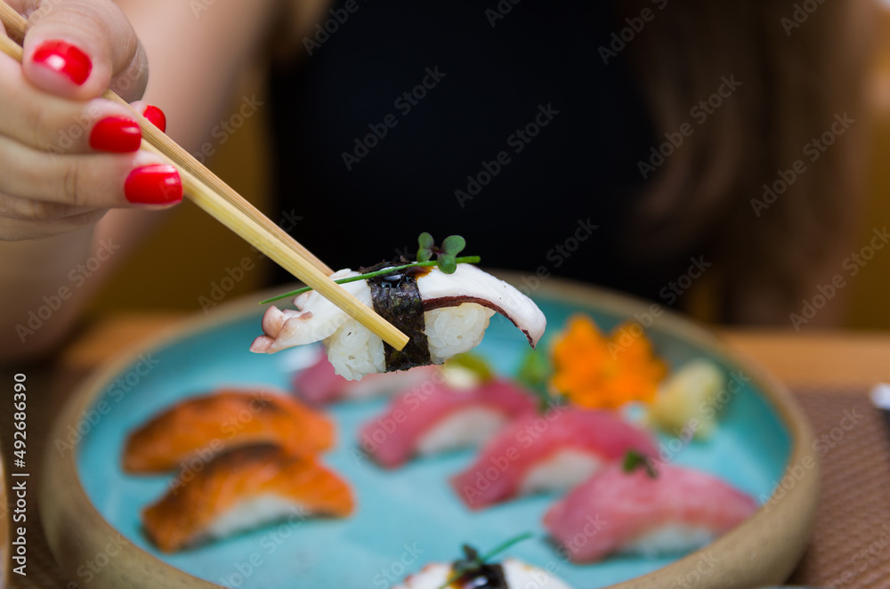 Obraz premium Woman eating delicious sushi, closeup on chopsticks.