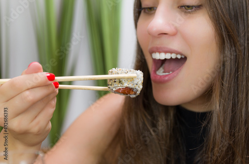 Woman eating delicious sushi, closeup on chopsticks.