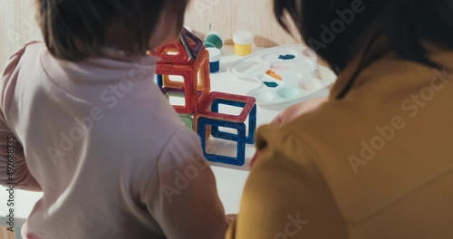 Child with his mother collects a magnetic constructor, a close up shot, a rear view, no faces are visible. The concept of development, joint family pastime and education of the child in a playful way
