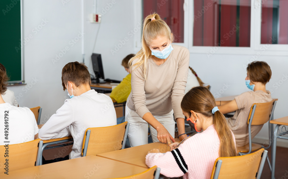 Fototapeta premium Woman teacher in face mask explaining new theme to children during class in primary school indoors