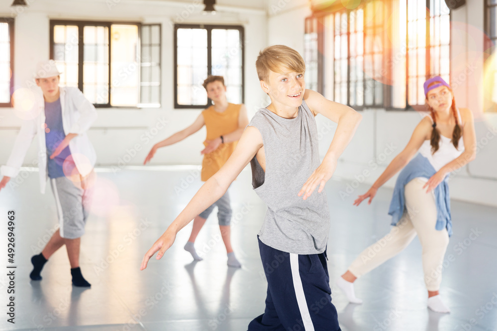 Fototapeta premium Emotional teen boy practicing active dance movements with friends at group dance class