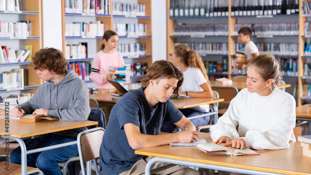 Obraz premium Cute tween girl and intelligent boy studying together in school library, reading books