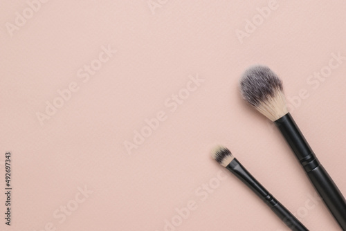 Two makeup brushes on a light beige background. Flat lay.