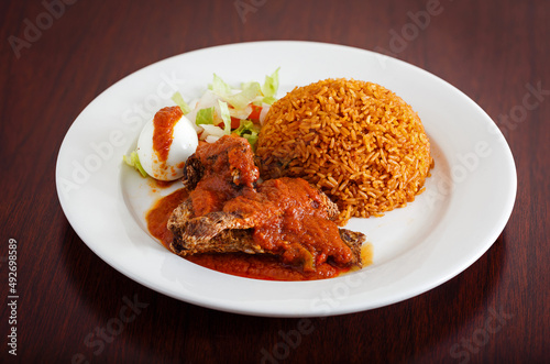 West African entree of jollof rice with fish and salad in a white plate