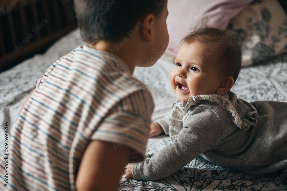 Brother sitting with his baby sister while the mother is not at home having fun lying on the bed. Baby care. Family care. Brother sitting with his baby sister while the mother is not at home having fun lying on the bed. Baby care. Family care.