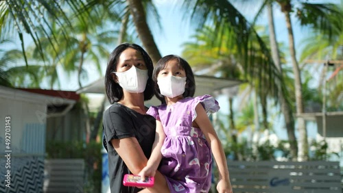Asian Asia mother carrying daughter walking at sentosa, Singapore with mask on

