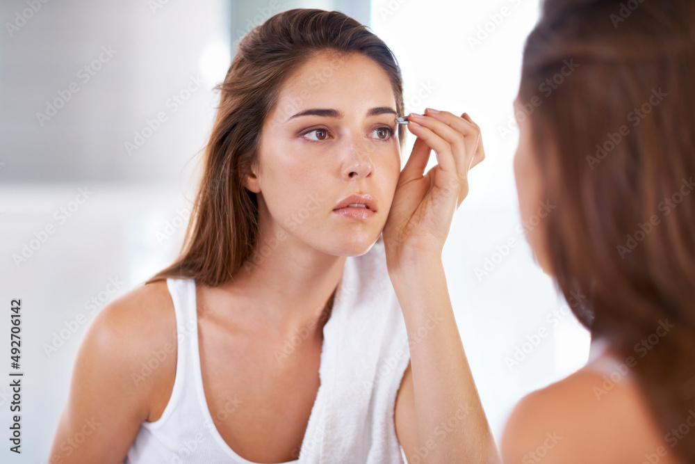 Shaping them to perfection. A young woman tweezing her eyebrows in front of a mirror. Shaping them to perfection. A young woman tweezing her eyebrows in front of a mirror.