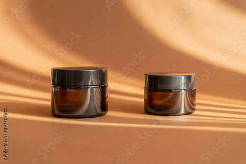 Obraz na płótnie Two jars of amber glass for cosmetics on brown background with shadow in form of stripes