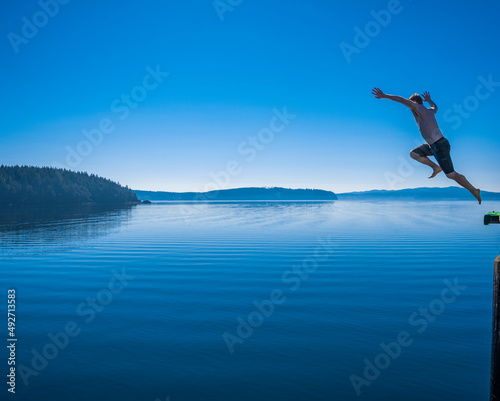 Adventurous athletic man jumping off a pier into a body of calm water. © Pelo Blanco Photo