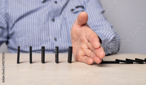 Domino effect stopping. Businessman hand closeup protecting domino pieces from falling. Successful intervention in business performance. High quality photo