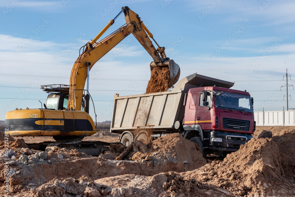 A powerful crawler excavator loads the earth into a dump truck against the blue sky. Development and removal of soil from the construction site. A powerful crawler excavator loads the earth into a dump truck against the blue sky. Development and removal of soil from the construction site.