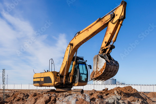 A powerful caterpillar excavator digs the ground against the blue sky. Earthworks with heavy equipment at the construction site.