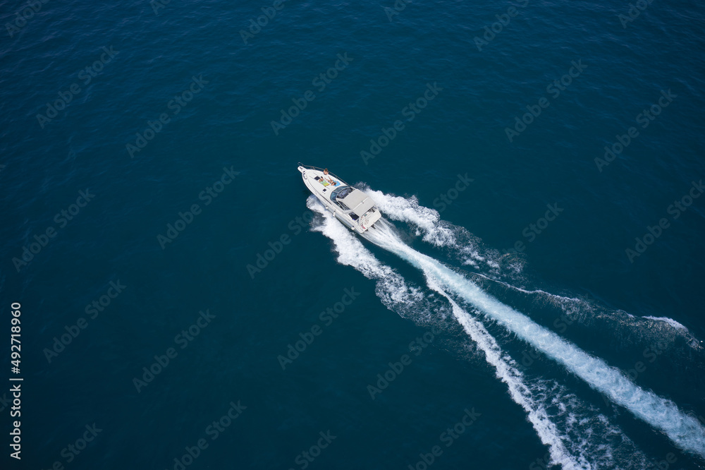 Modern boat in motion making a trail on the water top view. One boat on blue water drone view. Boat moving fast aerial view.