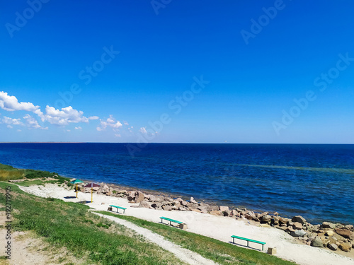 Seascape with coastline with empty benches, stone mound and deep blue sea on a sunny summer day. City beach in the city of Henichesk. Sea shore line with water surface. View point.