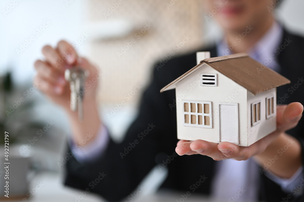 Young real estate agent man holding house model and keys. Real estate investment and insurance concept. Young real estate agent man holding house model and keys. Real estate investment and insurance concept.