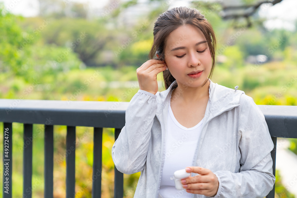 Asian woman listening to music from earphones and smartphone application while jogging at city park i summer morning. Healthy female athlete enjoy outdoor sport training workout exercise and running