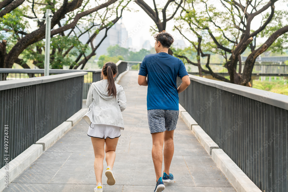 Happy family Asian couple in sportswear jogging exercise together at city public park in summer morning. Healthy man and woman enjoy outdoor lifestyle activity sport training fitness running workout