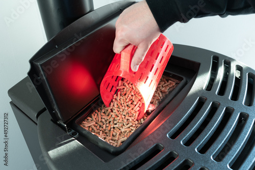 Close-up on pellets, black domestic pellet stove, man loading by hand granules with a red 3 d printed cup