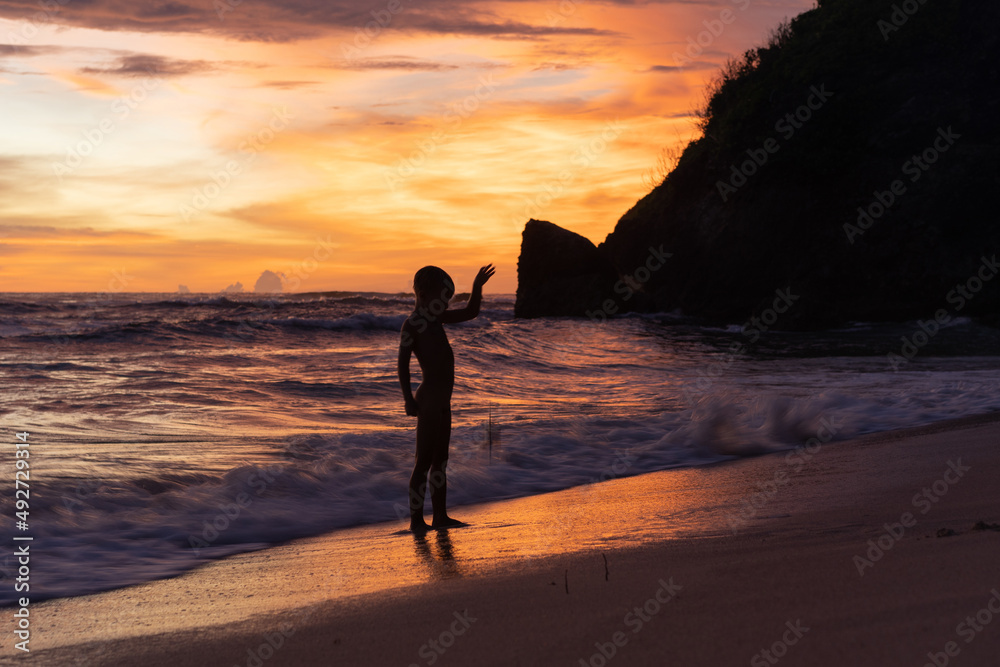 Fototapeta premium Child boy on the ocean at sunset, happy childhood, unity with nature, harmony.