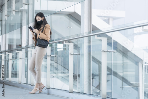 Asian woman walks up the elevator and plays with her mobile phone to shop in the mall.