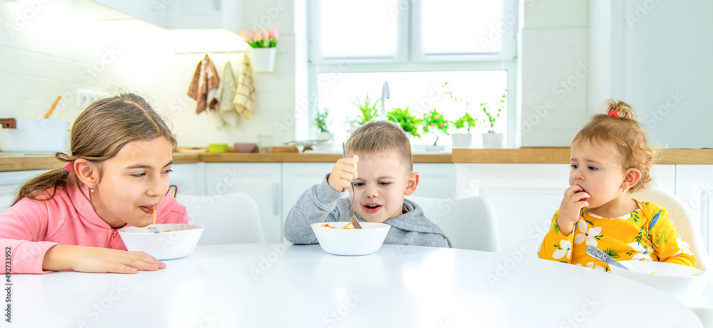 children in the kitchen at the table turning pasta. children in the kitchen at the table turning pasta.
