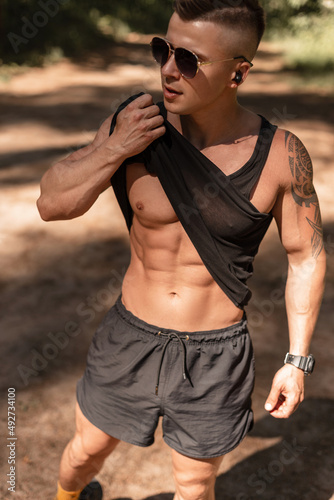 Fitness handsome man with sexy muscular body in black t-shirt and shorts walks in the park
