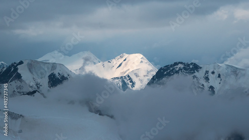 Wonderful minimalist panoramic landscape with big snowy mountain peaks above low clouds. Atmospheric minimalism with large snow mountain tops in cloudy sky.