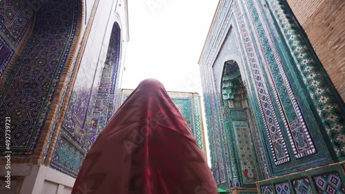 Muslim woman in a headscarf looks at a beautiful mosque in Samarkand. View from the rear