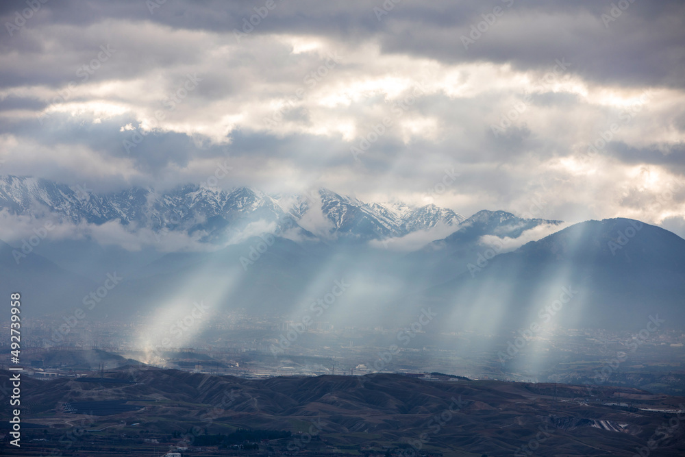 Sun light piercing through the clouds and hitting the mountains