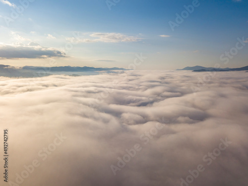 Flight over fog in Ukrainian Carpathians in summer. Mountains on the horizon. A thick layer of fog covers the mountains with a continuous carpet. Aerial drone view.