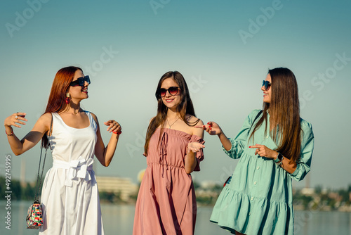 Group of cheerful happy girlfriends enjoying walk on embankement on summer day photo
