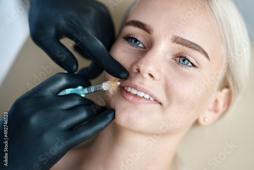 Botox injection in the lips, face close up and black doctor's gloves with a syringe