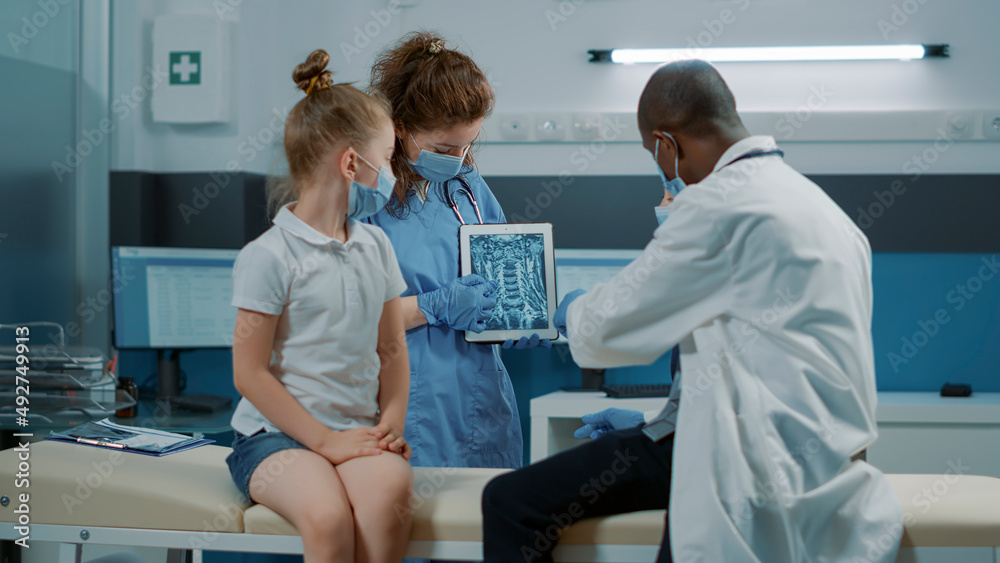 Diverse medical team explaining x ray scan diagnosis to little girl at