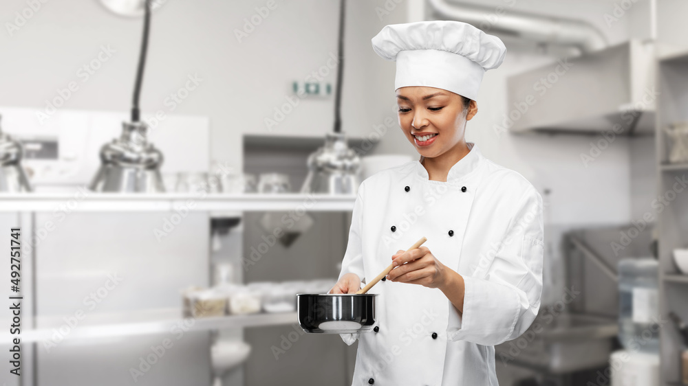 culinary and people concept - happy smiling female chef in toque and jacket with saucepan cooking food over restaurant kitchen background