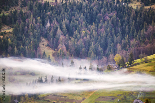 Beautiful spring landscape. Traditional mountain village on hills. Rural Ukraine Carpathian sunrise. Smoke from house. Clouds of fog