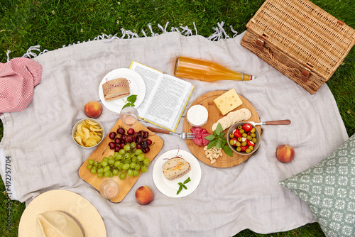 leisure, food and drinks concept - close up of snacks and picnic basket on blanket on grass at summer park photo