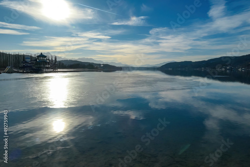 View on Woerthersee in Poertschach in Carinthia, Austria.The calm surface of the lake is reflecting the mountains, sunbeams and clouds. Clear and sunny day. Karawanks mountain range. Alps, Lake Woerth