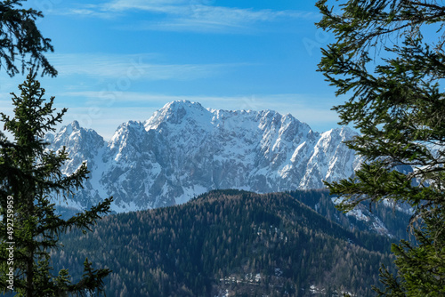Scenic view of snow capped mountain peaks of Karawanks on the way to Sinacher Gupf in Carinthia, Austria. Mount Wertatscha is visible through dense forest in early spring. Rosental on a sunny day.Hike photo